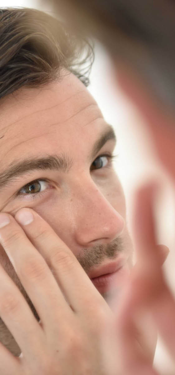Immagine di un uomo che si sta guardando allo specchio e con una mano si sta toccando l'occhio